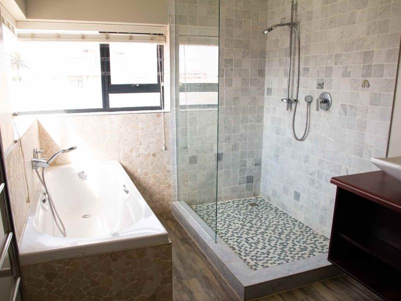 Modern bathroom featuring a walk-in shower with mosaic tiling, a built-in bathtub, a vessel sink vanity, and a heated towel rail.