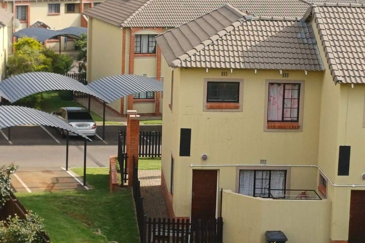 An elevated view of a townhouse complex featuring tiled roofs, paved parking areas with carports, and communal garden spaces.