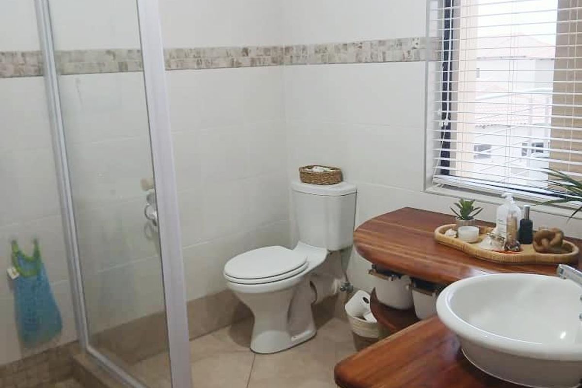 A functional bathroom featuring a glass-enclosed shower, a white ceramic toilet, and a wooden vanity with a modern vessel sink.