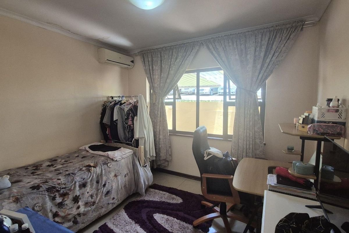 A functional bedroom featuring a wall-mounted air conditioning unit and a large window providing natural light.