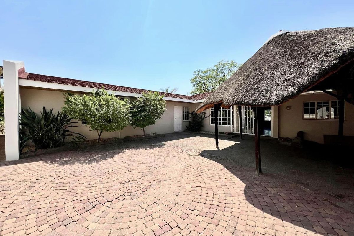 A spacious paved courtyard featuring a traditional thatch-roofed outdoor entertainment area and established garden beds.