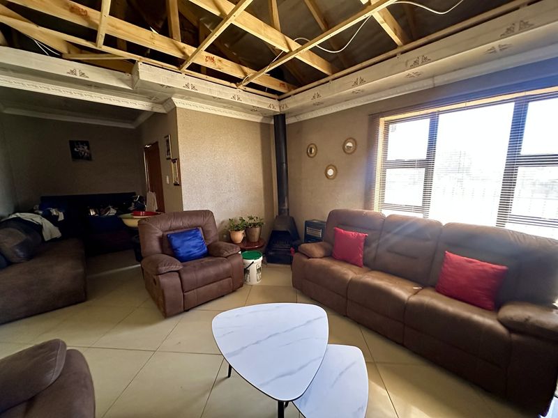 Living room featuring a freestanding fireplace, tiled floors, and decorative cornices, currently undergoing ceiling renovations with exposed timber roof trusses.