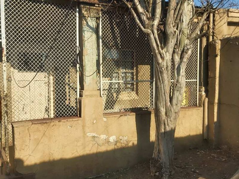 Rear exterior view of the property showing a weathered plastered wall, security mesh screens, and signs of significant structural deterioration.