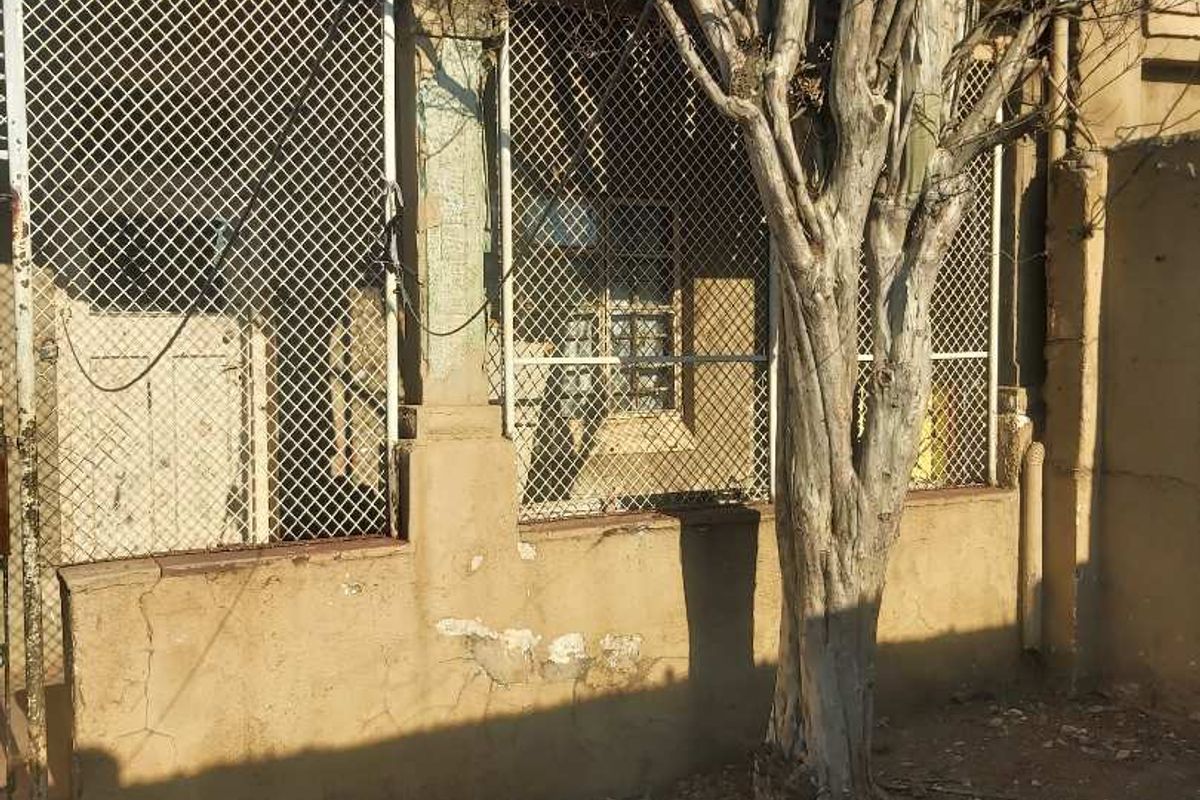 Rear exterior view of the property showing a weathered plastered wall, security mesh screens, and signs of significant structural deterioration.