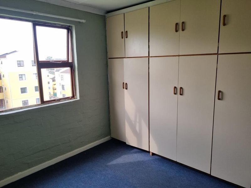 A vacant bedroom featuring built-in cupboards, carpeted flooring, and a window with natural light.