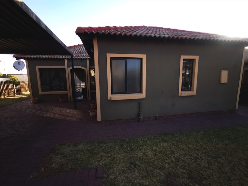 Rear view of the house featuring a paved patio area, tiled roof, and an attached carport structure.