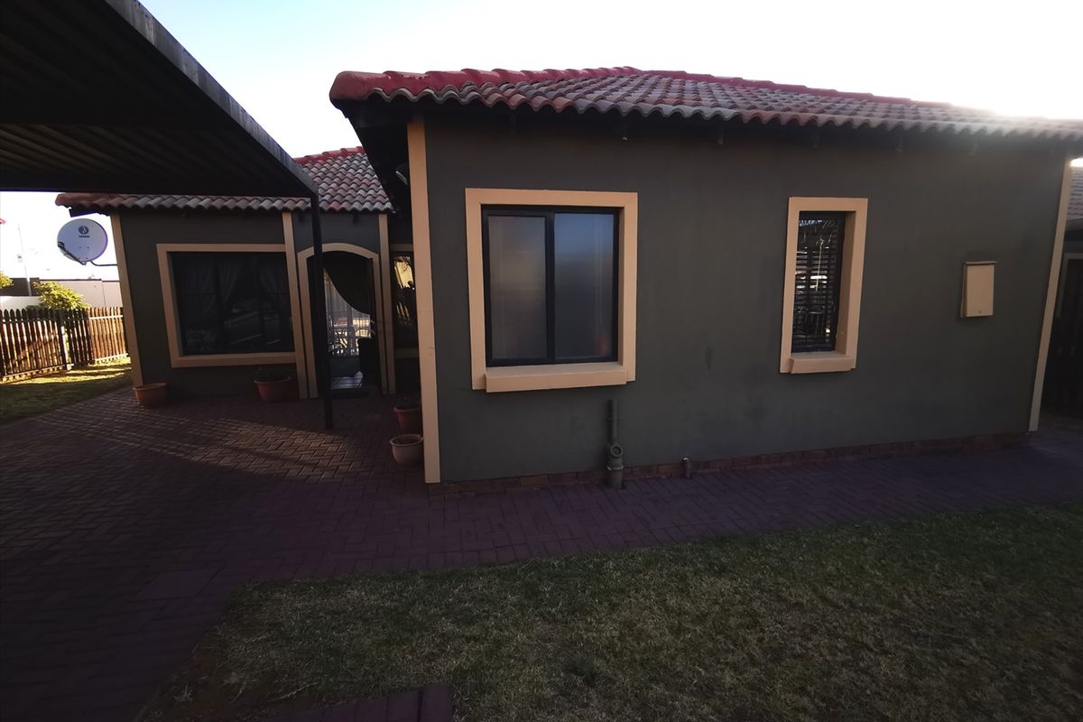 Rear view of the house featuring a paved patio area, tiled roof, and an attached carport structure.