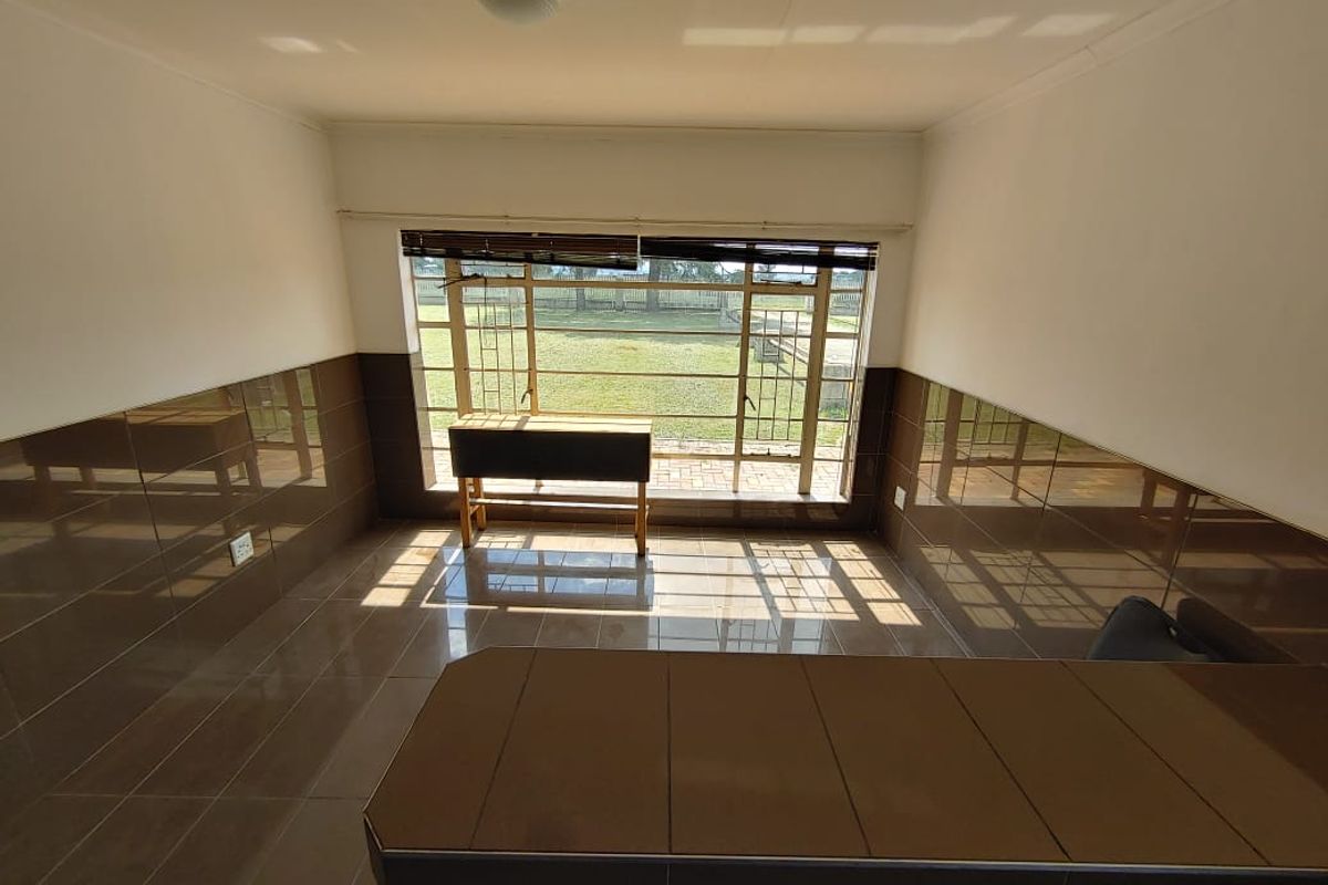 An empty living area featuring dated brown wall and floor tiles, a built-in counter, and a large window overlooking the garden.