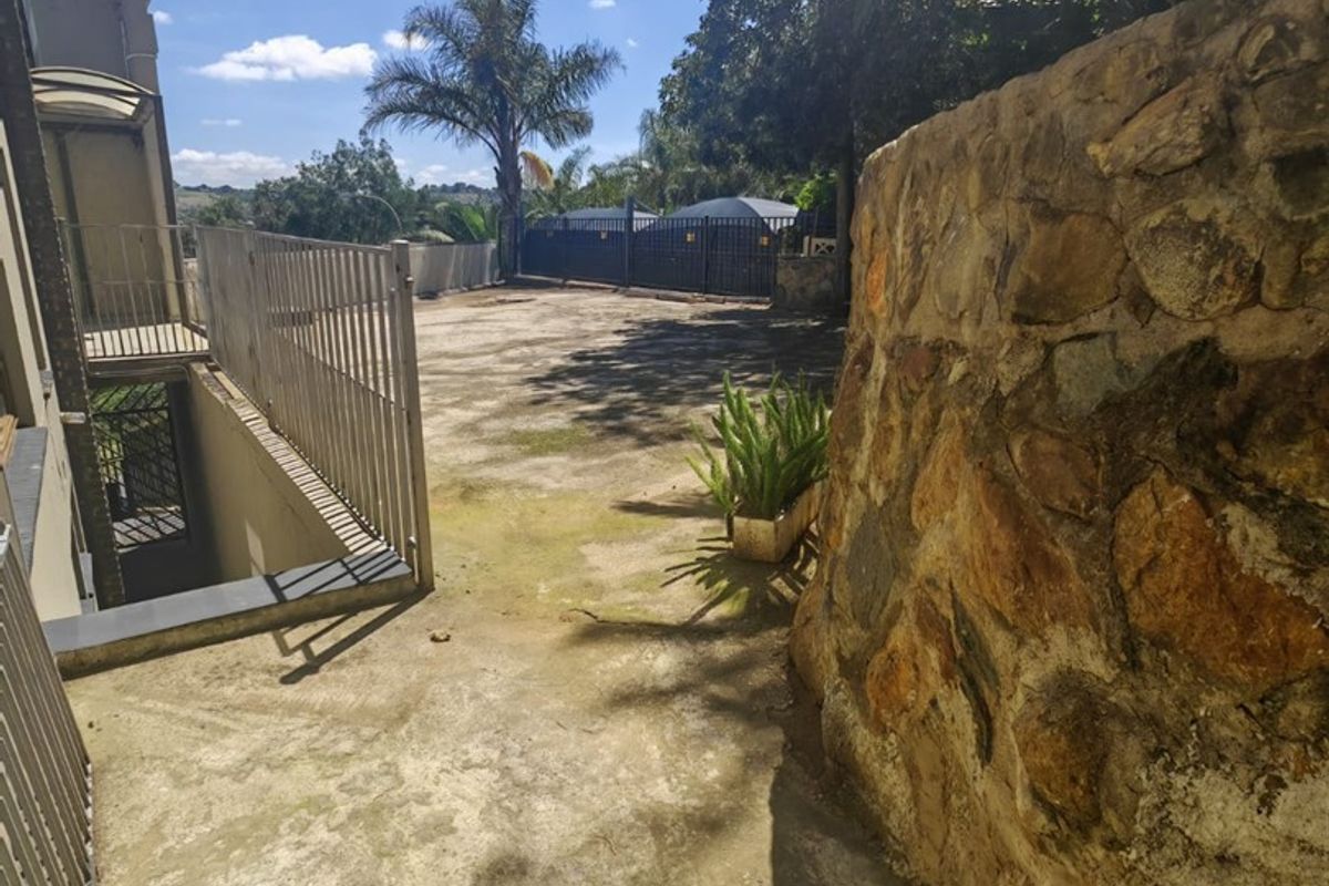 A rear outdoor area featuring a stone retaining wall, concrete paving, and metal security fencing, providing access to the lower level of the property.