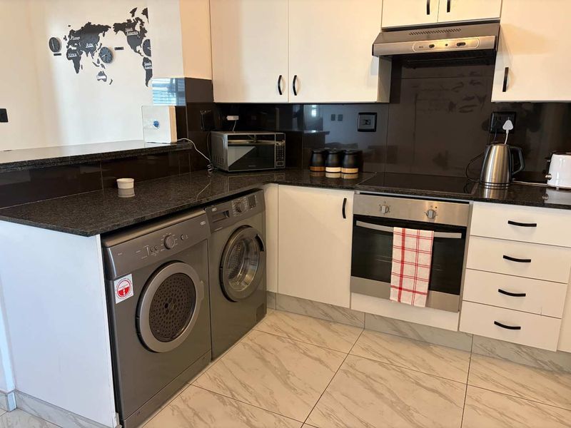 Modern kitchen featuring white cabinetry, dark granite countertops, built-in oven, electric hob, extractor fan, and tiled flooring with integrated laundry appliance space.