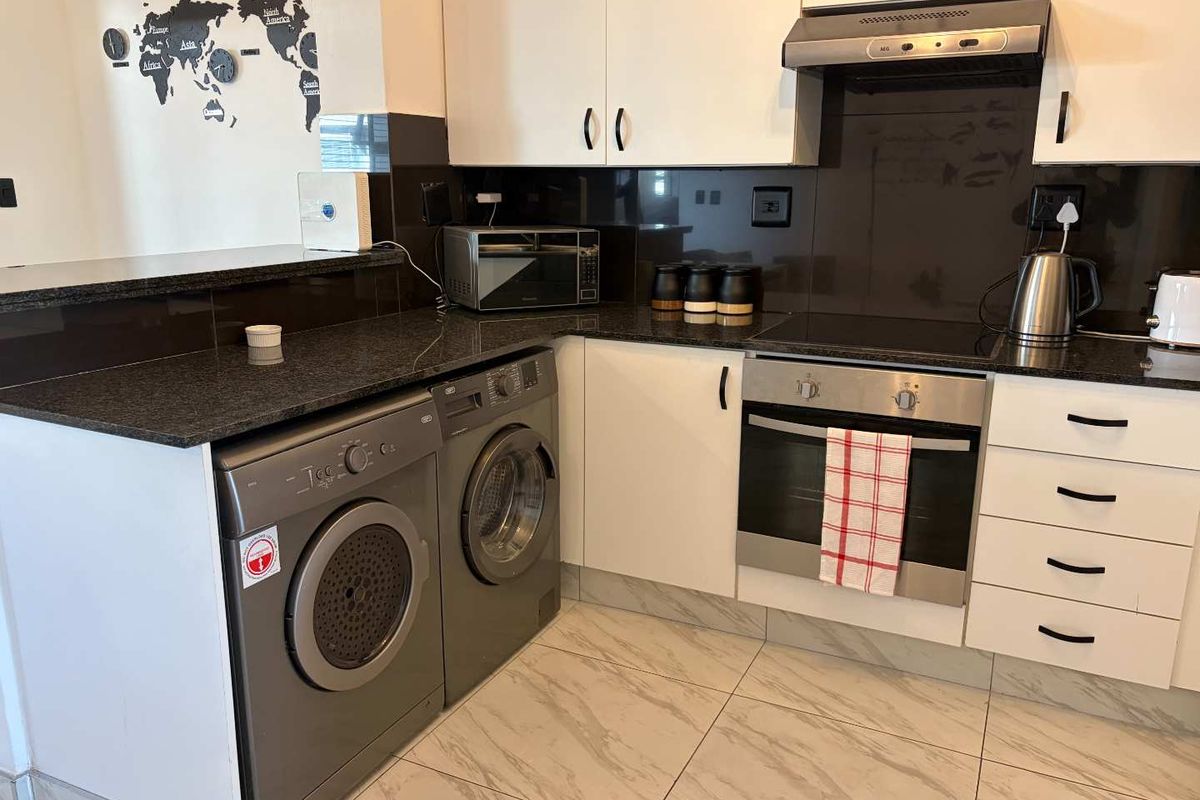 Modern kitchen featuring white cabinetry, dark granite countertops, built-in oven, electric hob, extractor fan, and tiled flooring with integrated laundry appliance space.