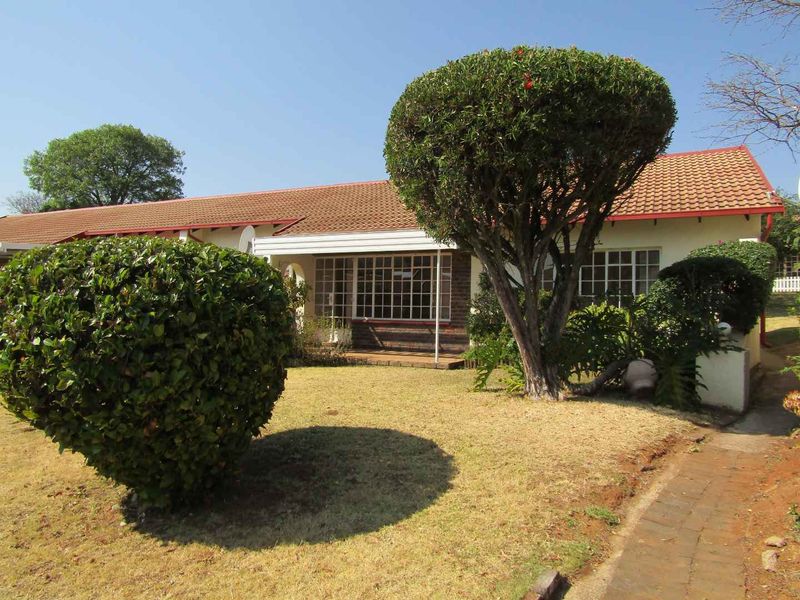 Front view of a retirement village unit featuring a tiled roof, brick facade, and a covered patio area with a paved walkway.