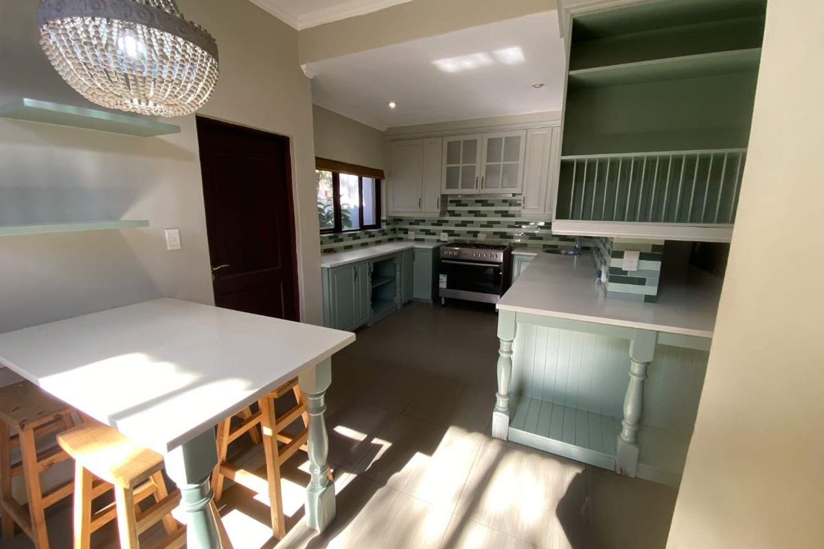 A well-lit kitchen featuring sage green cabinetry, white countertops, a gas stove, and a built-in breakfast nook with a decorative chandelier.