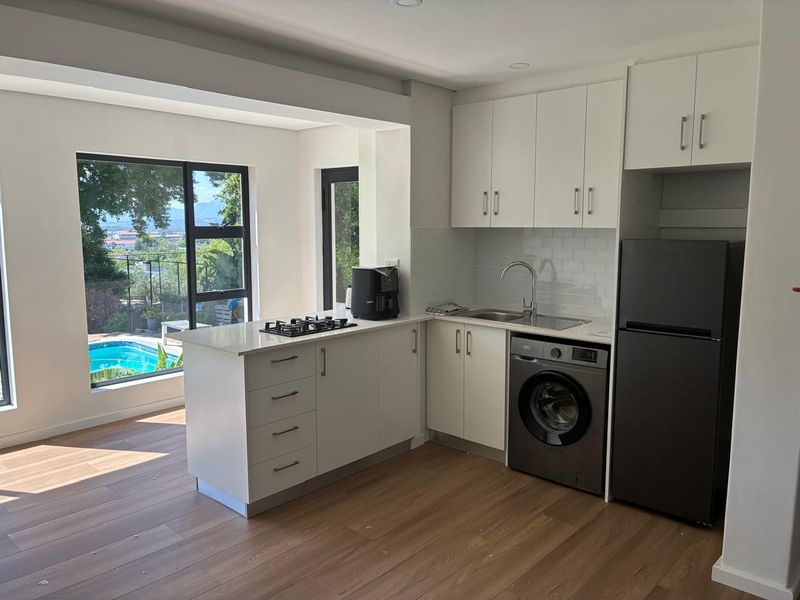 Modern kitchen featuring white cabinetry, subway tile backsplash, gas hob, and integrated laundry space, with large windows overlooking the pool area.
