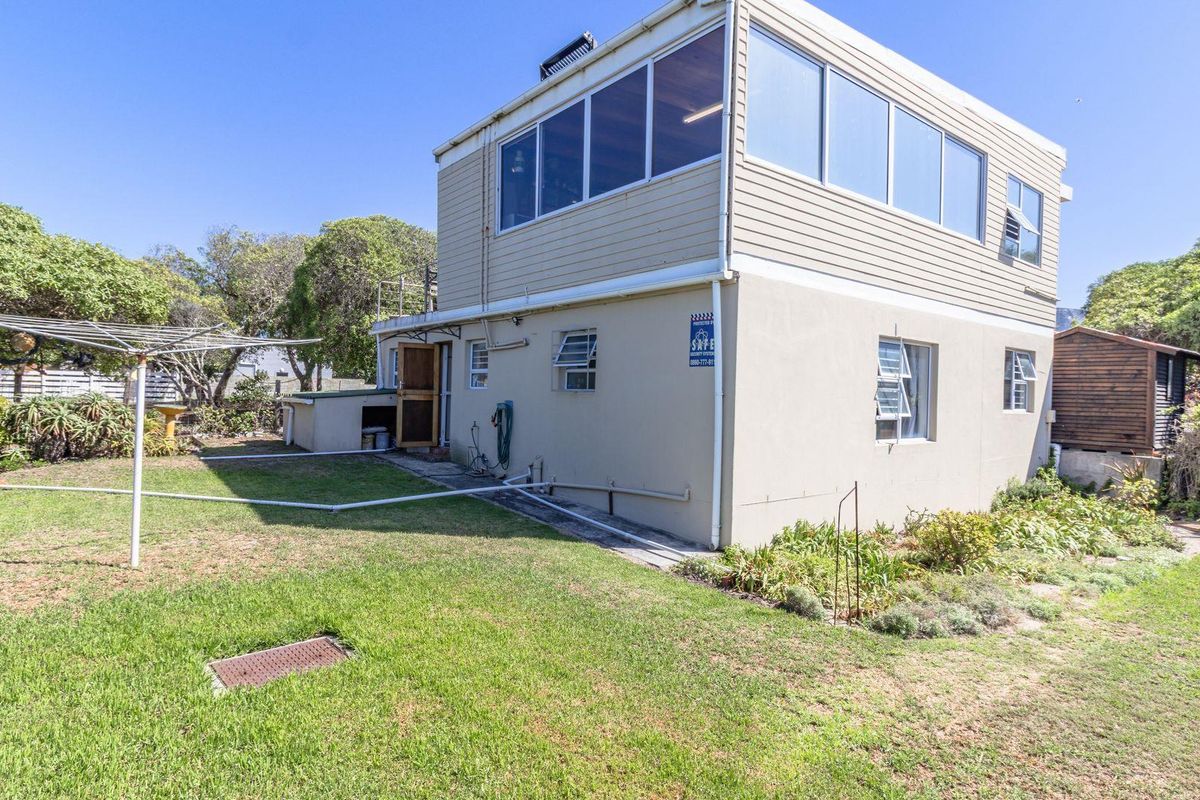 Rear view of a two-story residential property featuring plastered masonry walls, upper-level cladding, and solar water heating infrastructure set within a garden.