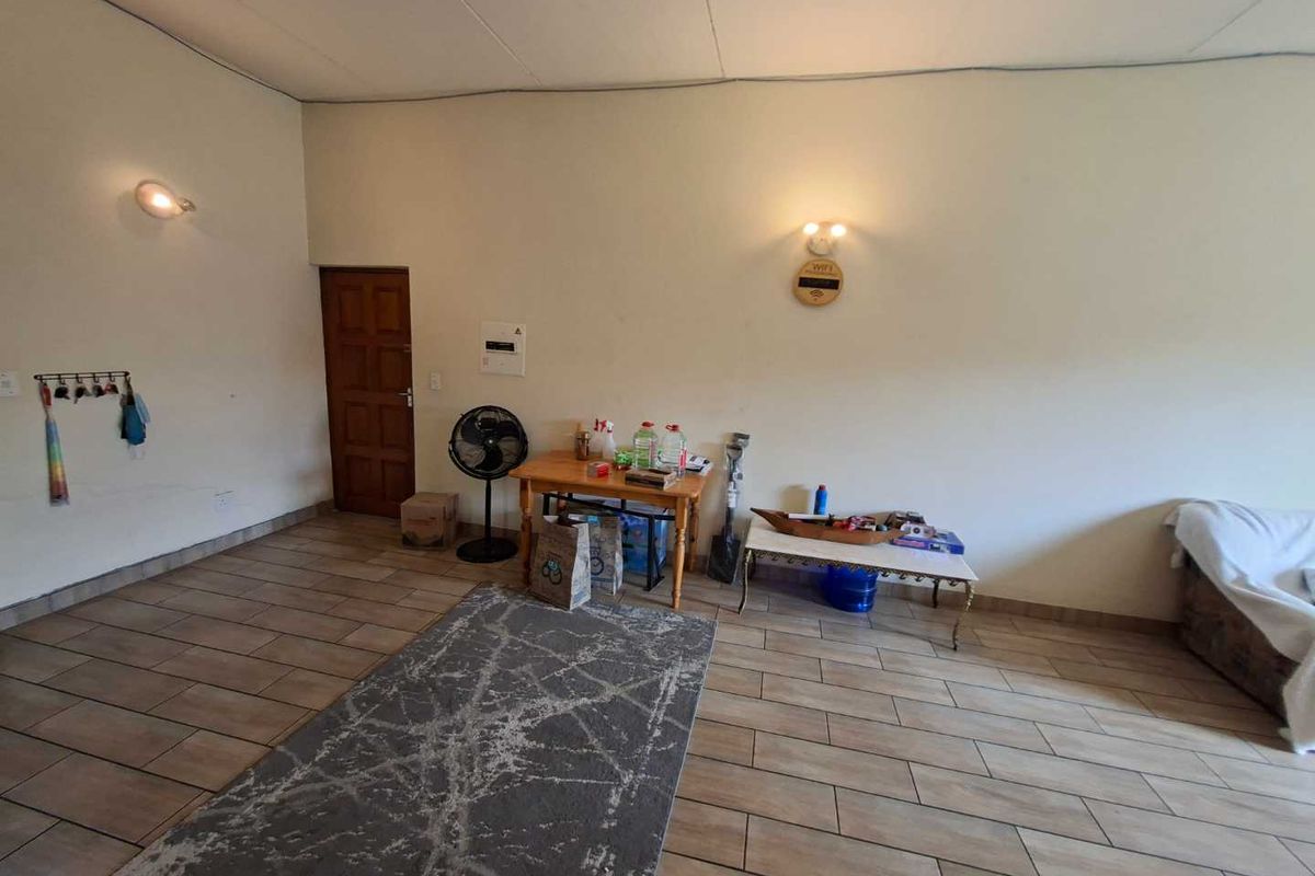 A spacious living area featuring tiled flooring, wall-mounted lighting fixtures, and a solid timber door, providing a neutral foundation for interior design.