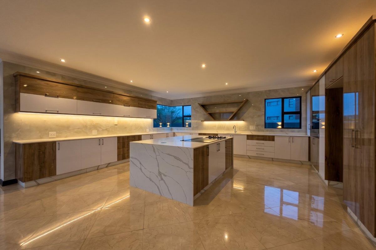 Modern, spacious kitchen featuring a large central island with stone countertops, sleek two-tone cabinetry, integrated cooktop, and polished marble-look flooring.