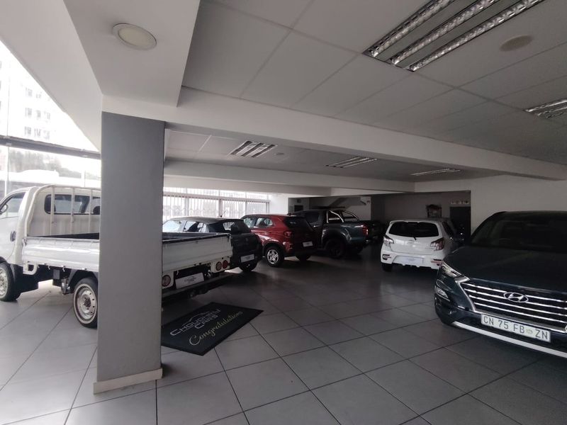 Spacious indoor showroom area featuring tiled flooring, structural support columns, and integrated ceiling lighting, suitable for vehicle display.