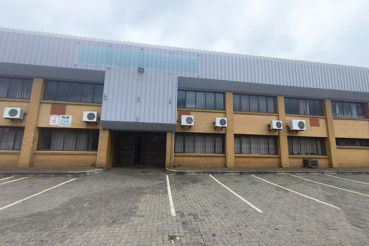 Front elevation of an industrial building featuring a brick facade, metal cladding, and dedicated paved parking spaces with multiple wall-mounted air conditioning units.