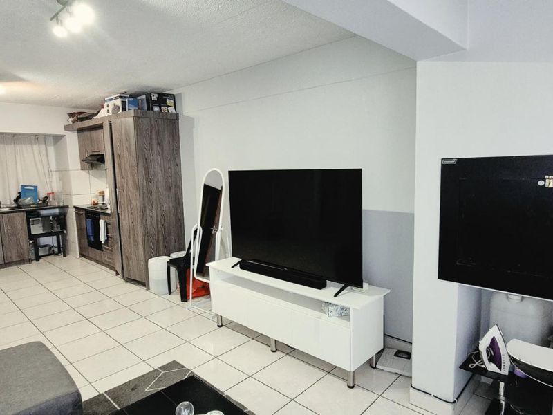 Open-plan living area featuring tiled flooring and a functional kitchen with built-in cabinetry, oven, and extractor fan.