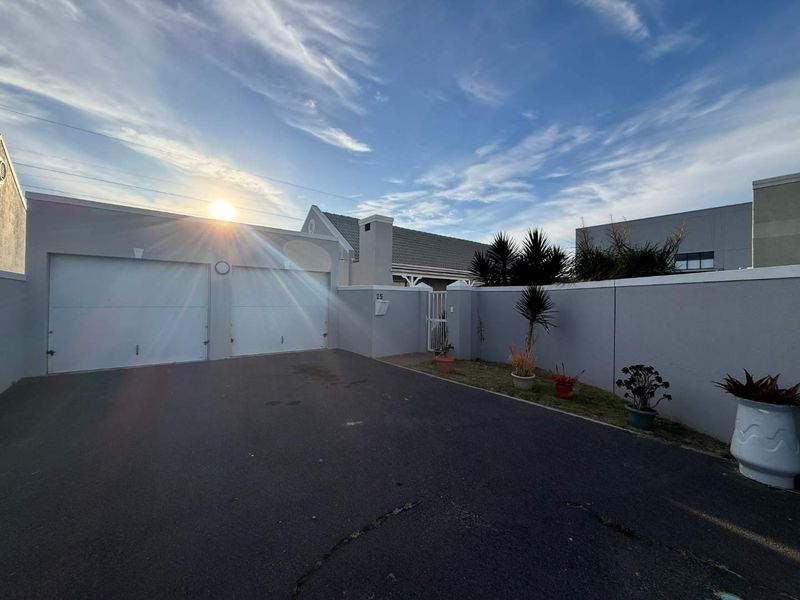 Front exterior view of the property featuring a double garage, secure boundary wall, and a paved driveway entrance.