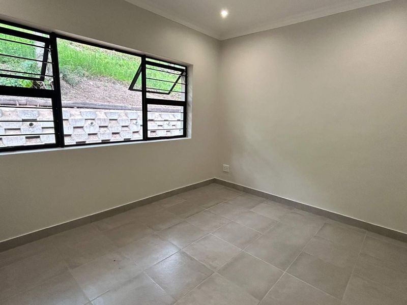 A clean, empty bedroom featuring neutral tiled flooring, modern aluminium window frames, and recessed downlighting, offering a blank canvas for personalization.