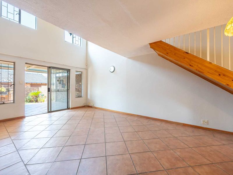 Spacious double-volume living area featuring tiled flooring, a staircase with a wooden handrail, and sliding glass doors leading to the outdoor patio.