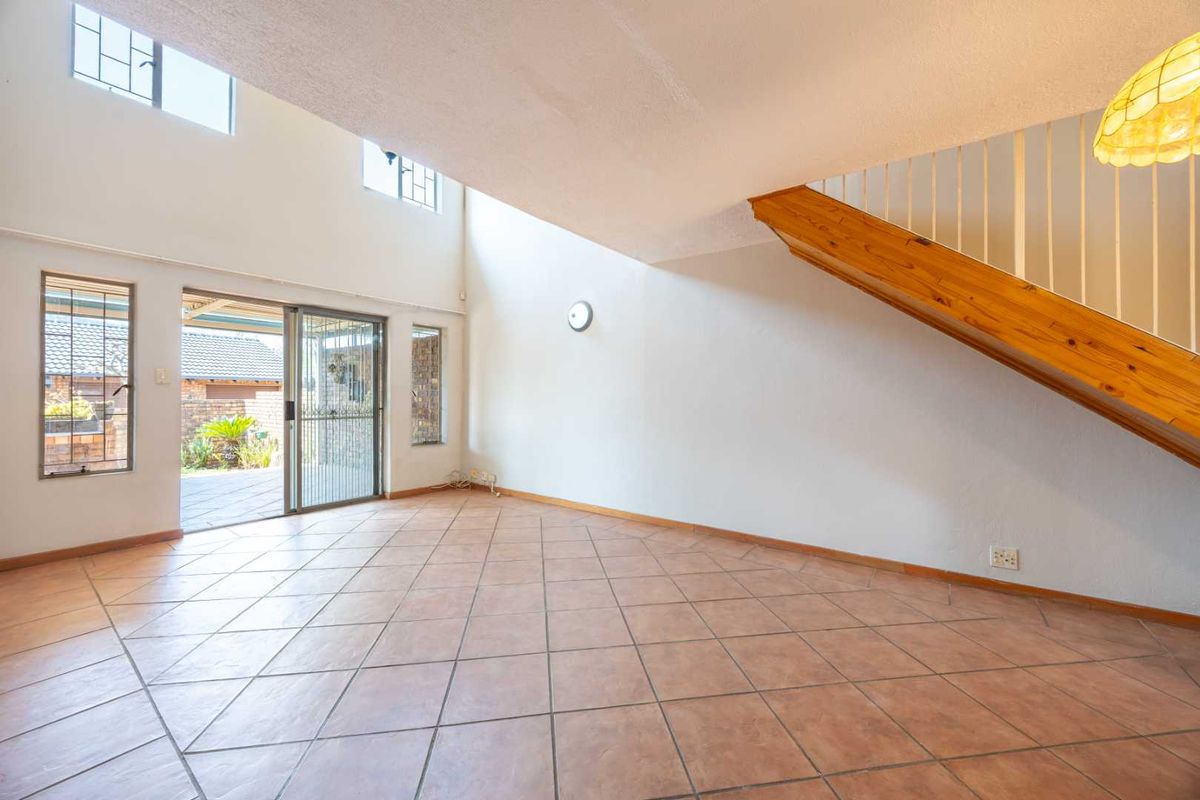 Spacious double-volume living area featuring tiled flooring, a staircase with a wooden handrail, and sliding glass doors leading to the outdoor patio.