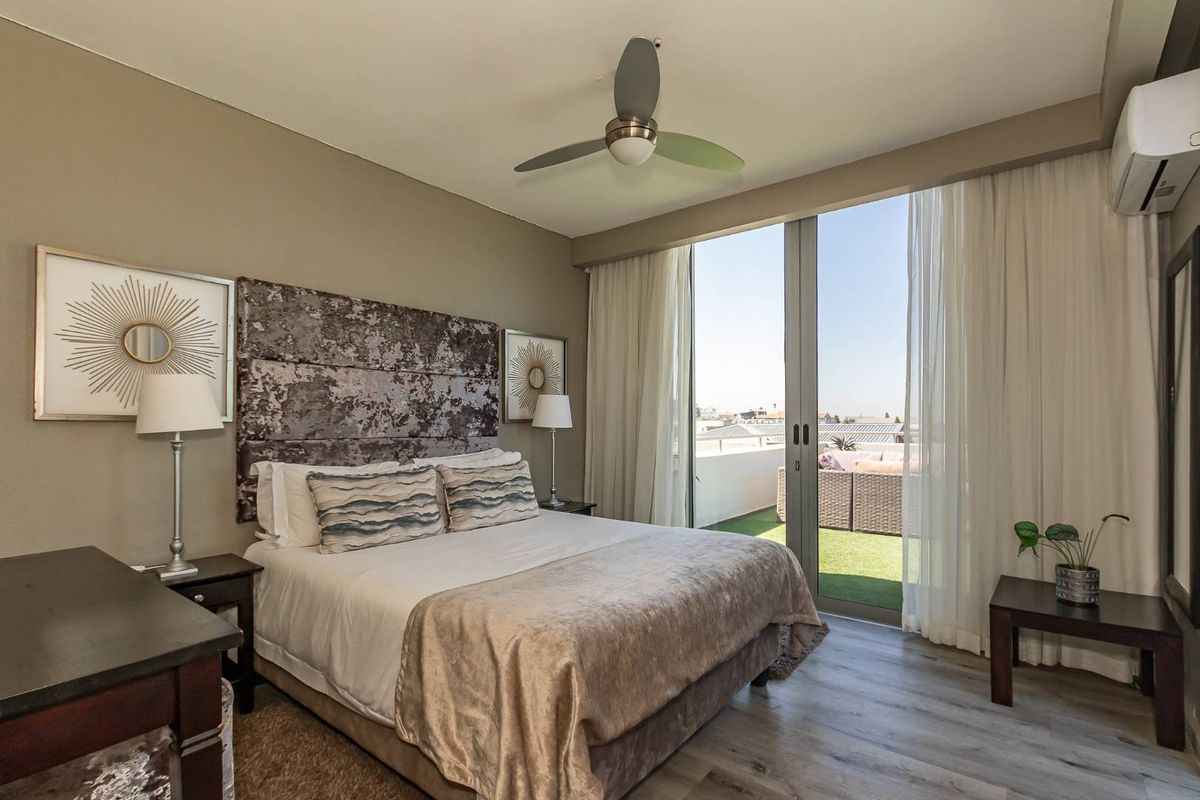 A well-maintained bedroom featuring wood-look flooring, a ceiling fan, wall-mounted air conditioning unit, and large sliding glass doors opening onto a private balcony.