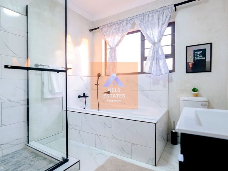 Modern bathroom featuring a glass-enclosed shower, a built-in bathtub with marble-look tiling, and a vanity unit.