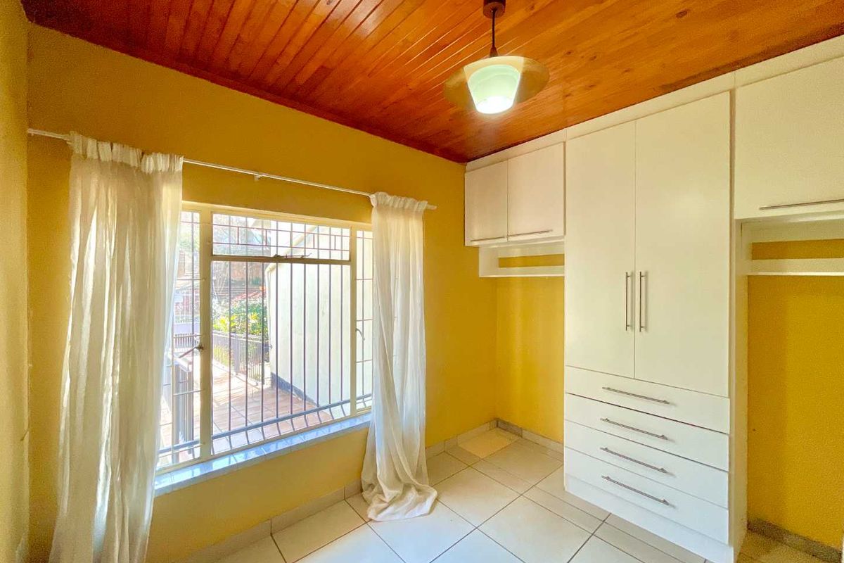 A bedroom featuring built-in white cabinetry, tiled flooring, and a timber-paneled ceiling with security bars on the window.