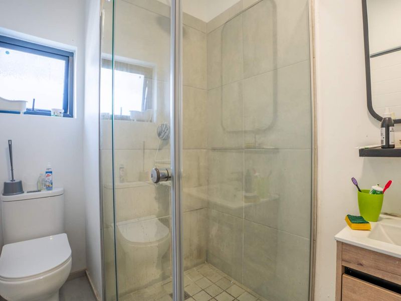 A functional bathroom featuring a glass-enclosed shower, vanity cabinet with integrated sink, and a toilet, illuminated by a small casement window.
