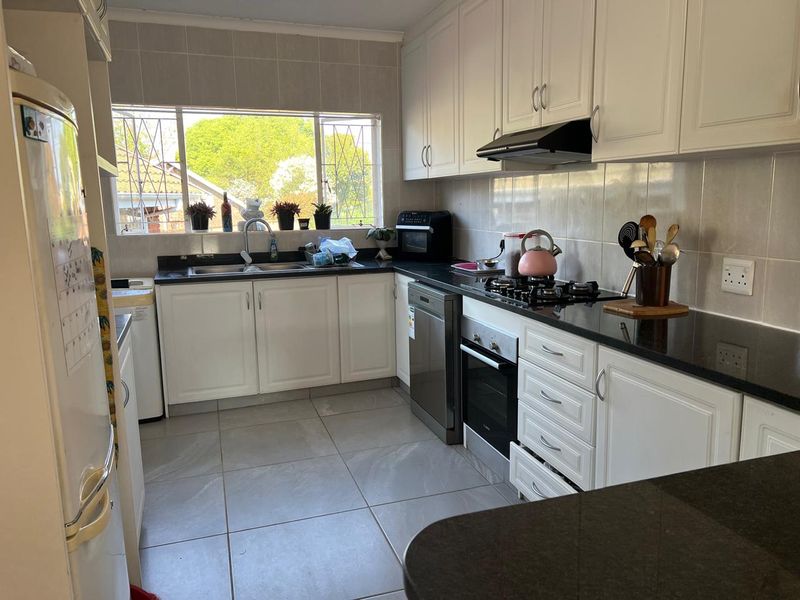 A functional kitchen featuring white cabinetry, granite countertops, a gas hob, built-in oven, and tiled flooring with ample natural light.