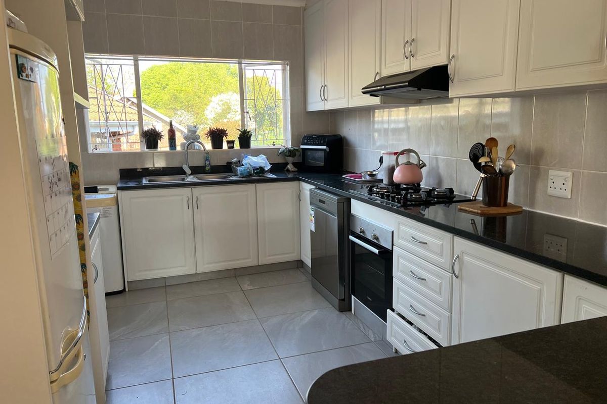 A functional kitchen featuring white cabinetry, granite countertops, a gas hob, built-in oven, and tiled flooring with ample natural light.
