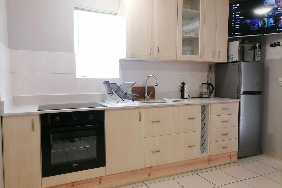 A functional kitchen featuring light wood cabinetry, a built-in electric oven and hob, tiled backsplash, and tiled flooring.