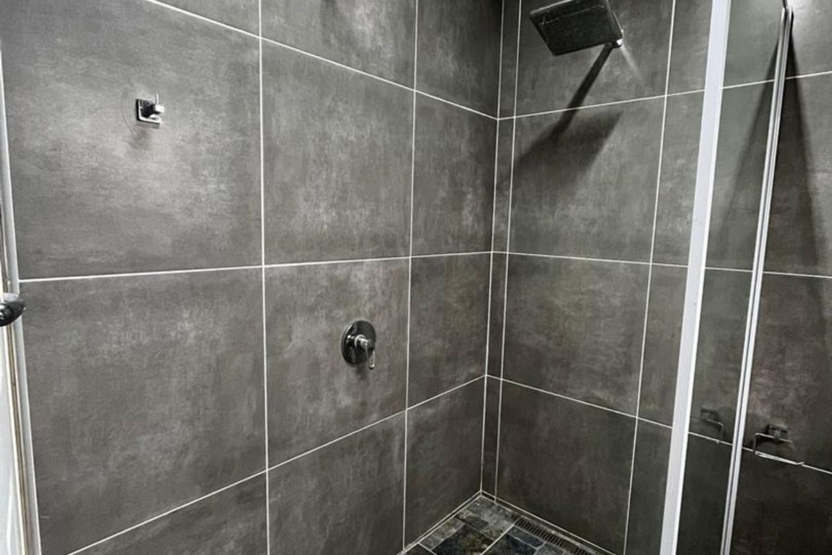 Modern walk-in shower featuring dark grey wall tiles, a textured stone-look floor, a fixed shower head, and a glass screen enclosure.