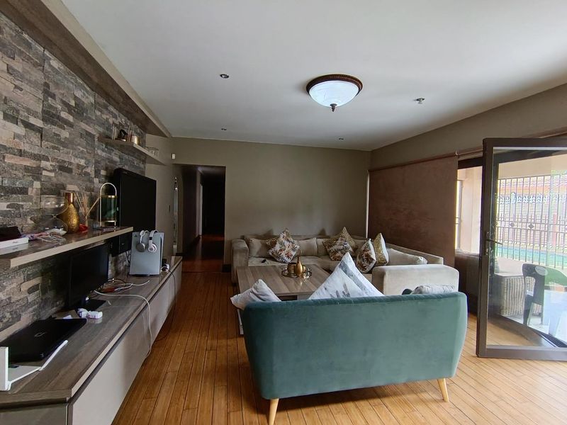 Spacious living room featuring a stone veneer accent wall, built-in cabinetry, hardwood flooring, and direct access to an outdoor patio area.