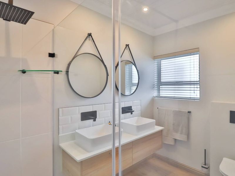 Modern bathroom featuring a double floating vanity with vessel sinks, matte black fixtures, subway tile backsplash, and a glass-enclosed rain shower.