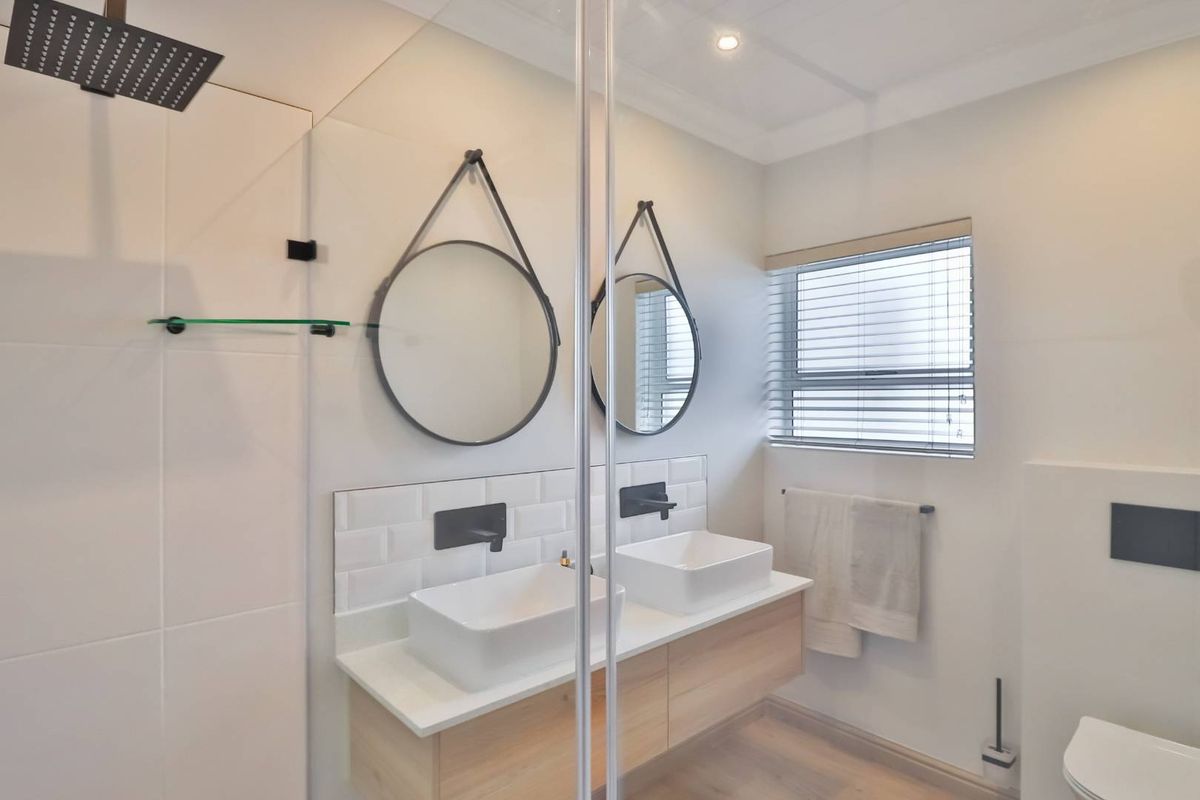 Modern bathroom featuring a double floating vanity with vessel sinks, matte black fixtures, subway tile backsplash, and a glass-enclosed rain shower.