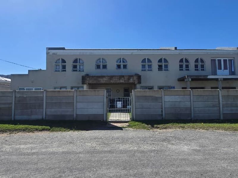 Front elevation of a two-story house featuring arched windows, a concrete facade, and a secure precast boundary wall with a metal entrance gate.