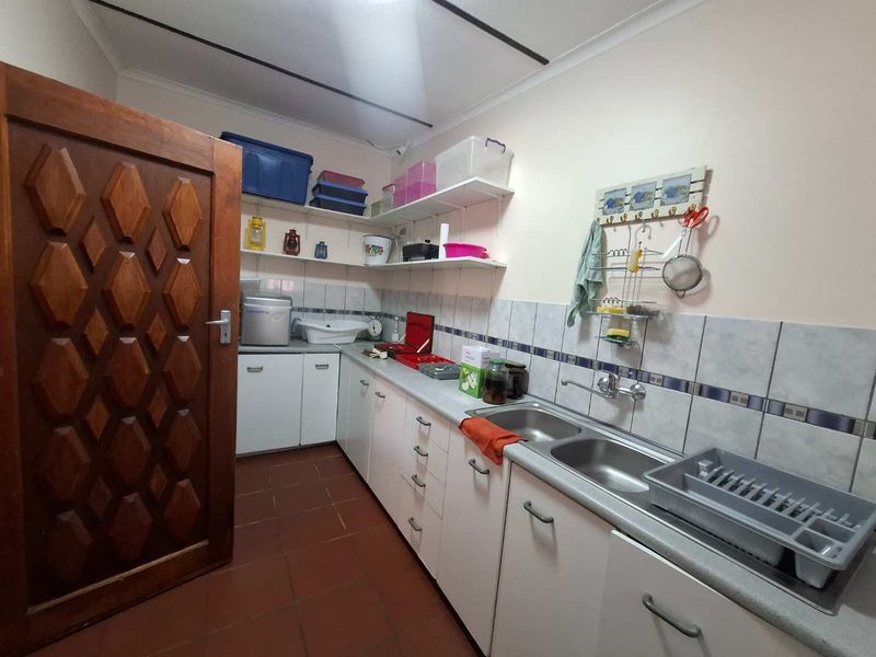 Functional scullery area featuring double stainless steel sink, tiled splashback, built-in cabinetry, and open shelving for additional storage.