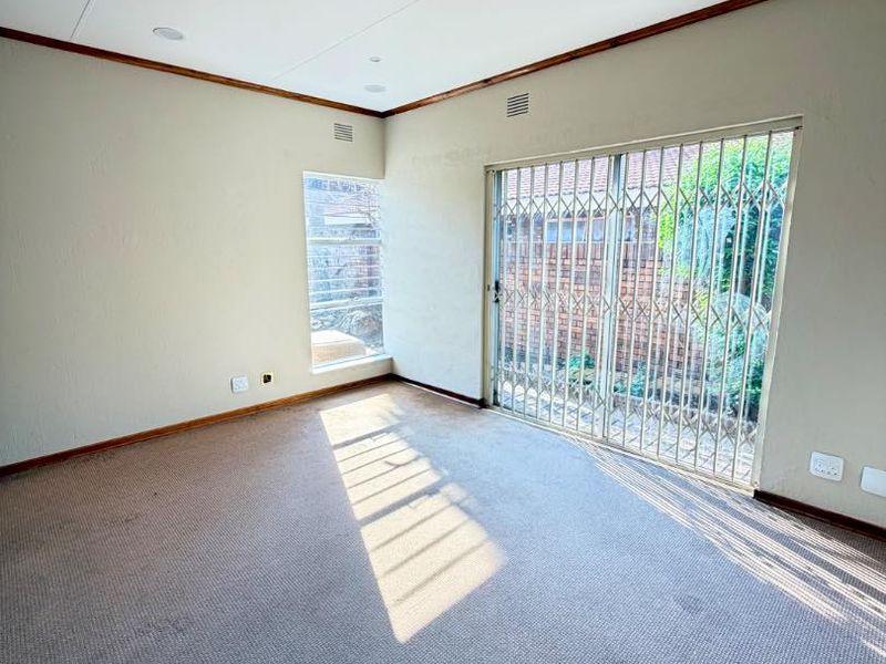 An empty living room featuring carpet flooring, recessed lighting, and a sliding glass door with a security gate leading to the exterior.