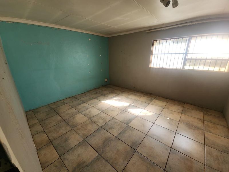 An empty bedroom featuring tiled flooring, a window with security bars, and painted walls in need of cosmetic attention.