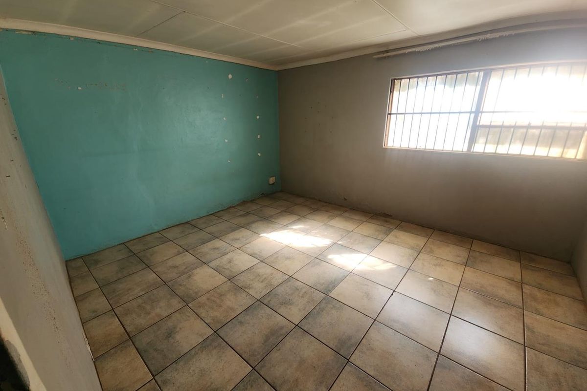An empty bedroom featuring tiled flooring, a window with security bars, and painted walls in need of cosmetic attention.