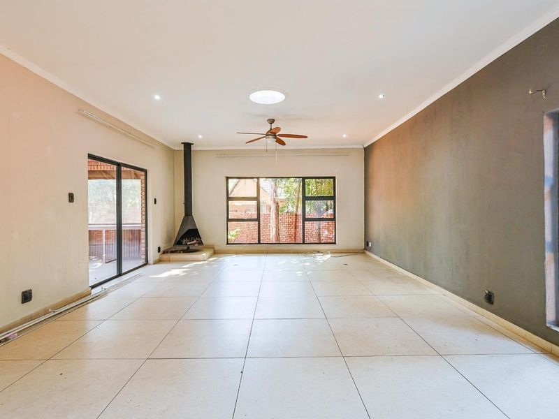 Spacious, empty living room featuring large tiled floors, a freestanding fireplace, ceiling fan, skylight, and sliding doors leading to an outdoor area.