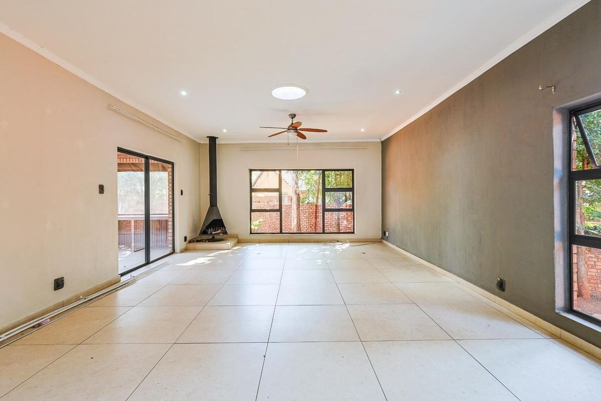 Spacious, empty living room featuring large tiled floors, a freestanding fireplace, ceiling fan, skylight, and sliding doors leading to an outdoor area.