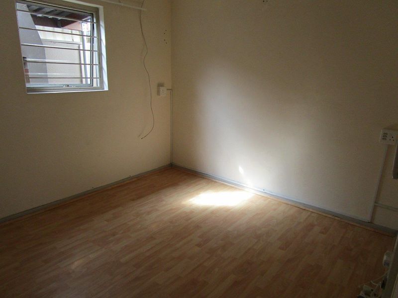 An empty bedroom featuring laminate flooring, a window with security bars, and visible electrical points, ready for a fresh update.