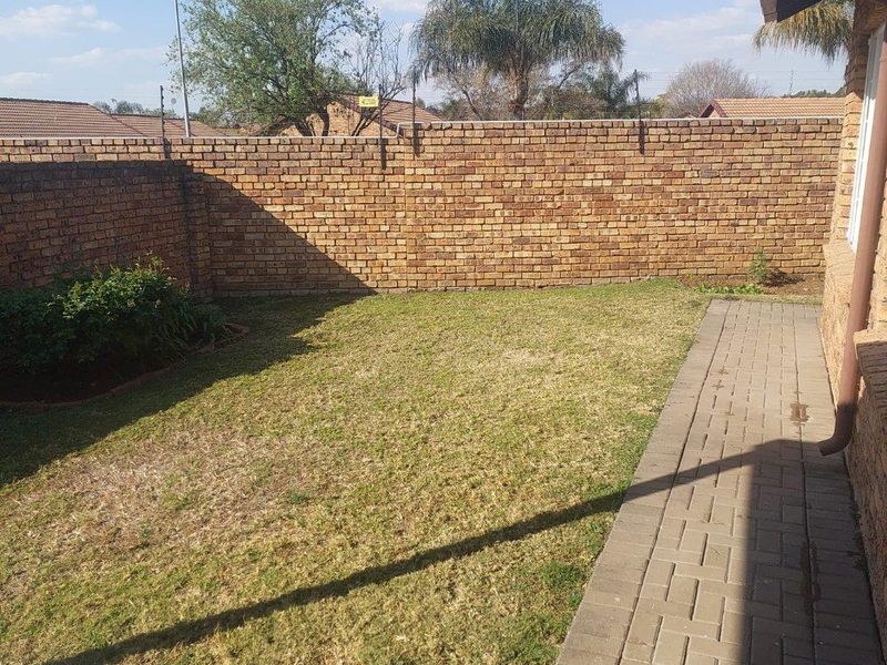 A private rear garden featuring a brick boundary wall, a paved walkway, and a lawn area.