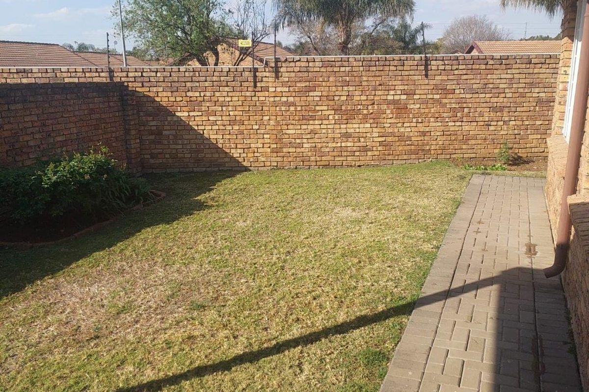 A private rear garden featuring a brick boundary wall, a paved walkway, and a lawn area.