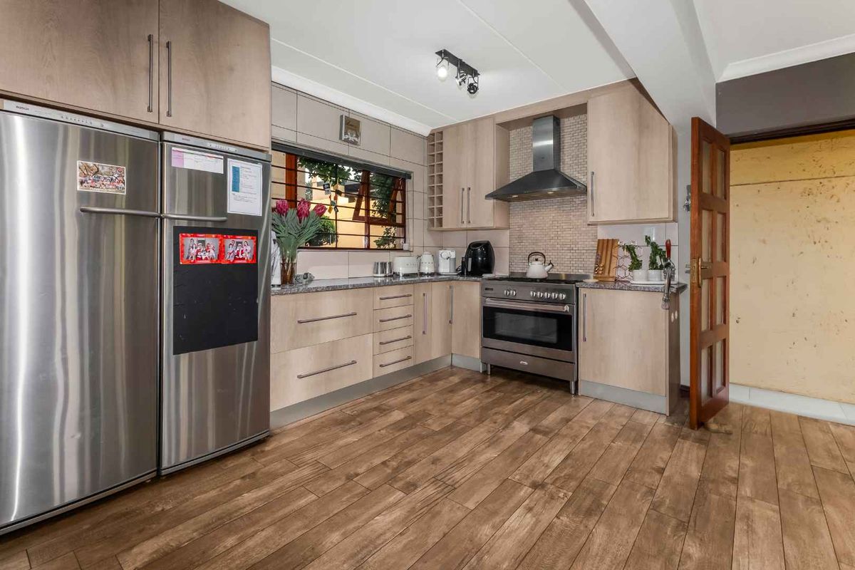 A functional kitchen featuring light wood cabinetry, granite countertops, a stainless steel extractor fan, and durable laminate flooring.